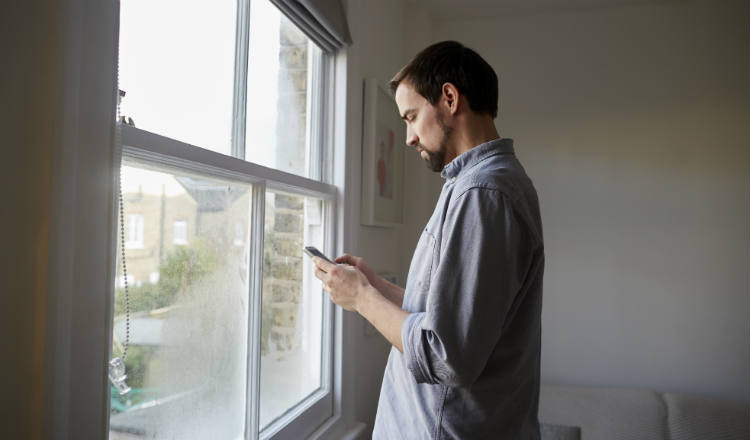 一个年轻人站在窗边看手机